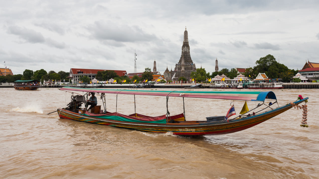 Wat Arun visto desde el otro lado del río Chao Phraya en Bangkok con un barco de cola larga pasando por delante