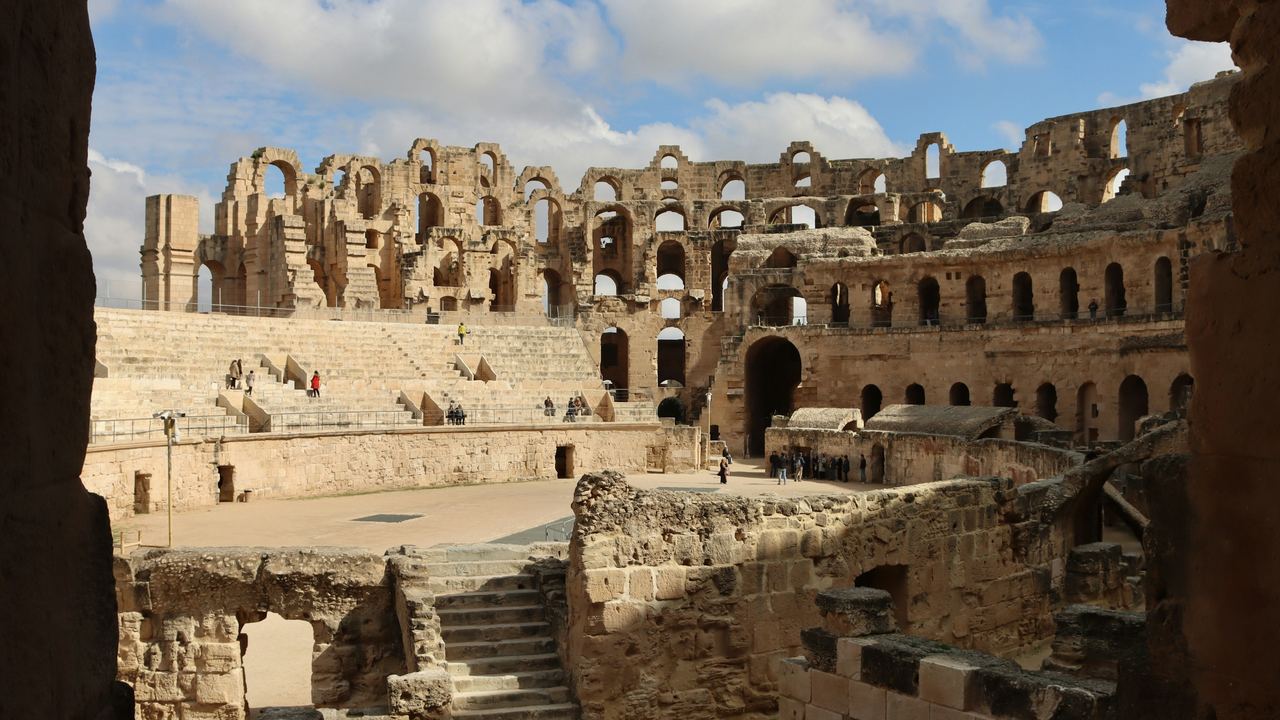 Gradinate e archi di pietra dell'anfiteatro romano di El Jem, in Tunisia, sotto un cielo blu