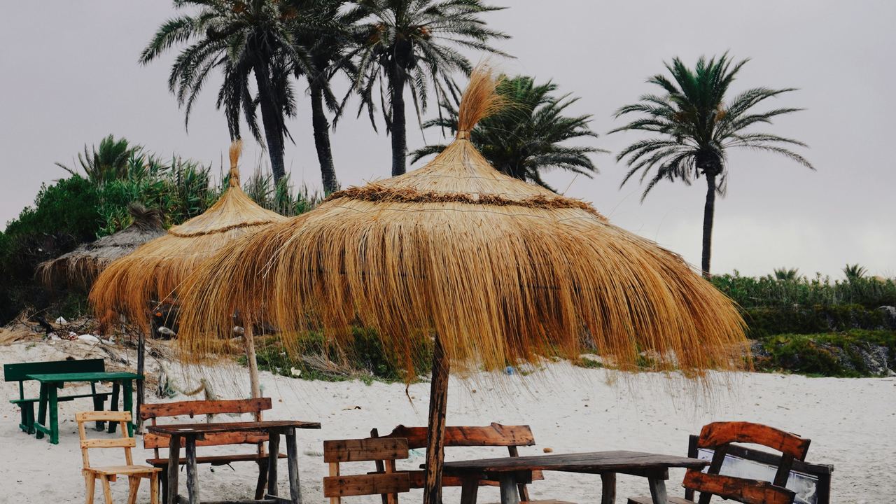 Ombrelloni di foglie di palma e panche di legno su una spiaggia di sabbia bianca vicino a Mahdia, in Tunisia