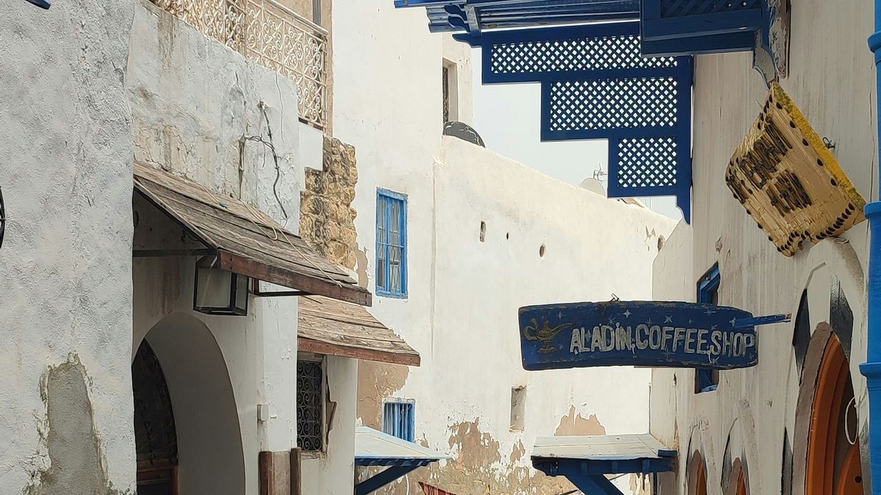 Vicolo stretto imbiancato a calce con persiane blu e un'insegna dipinta a mano nella medina di Sousse, in Tunisia