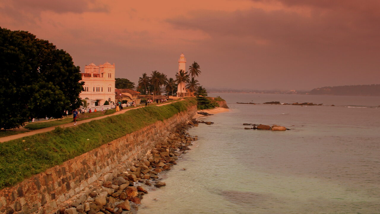 Det hvidkalkede fyrtårn og kokospalmerne på voldene i Galle Fort over havet i det sydlige Sri Lanka